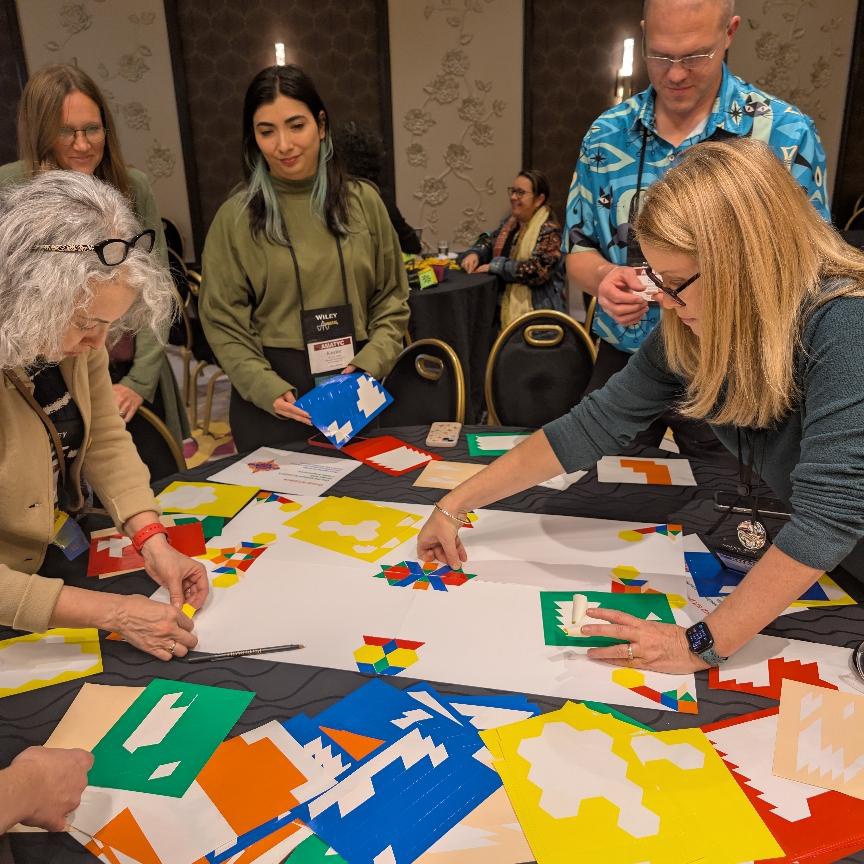 People at a table placing geometric shaped stickers onto posterboard.