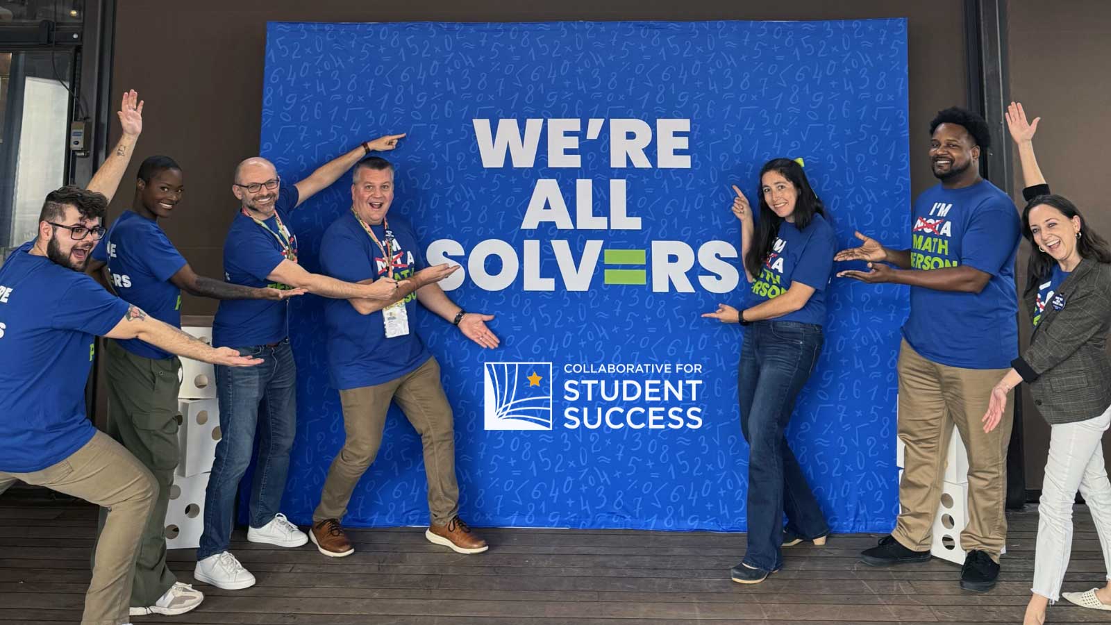 Group of smiling people pointing to a banner that reads: We're All Solvers. Collaborative for Student Success.